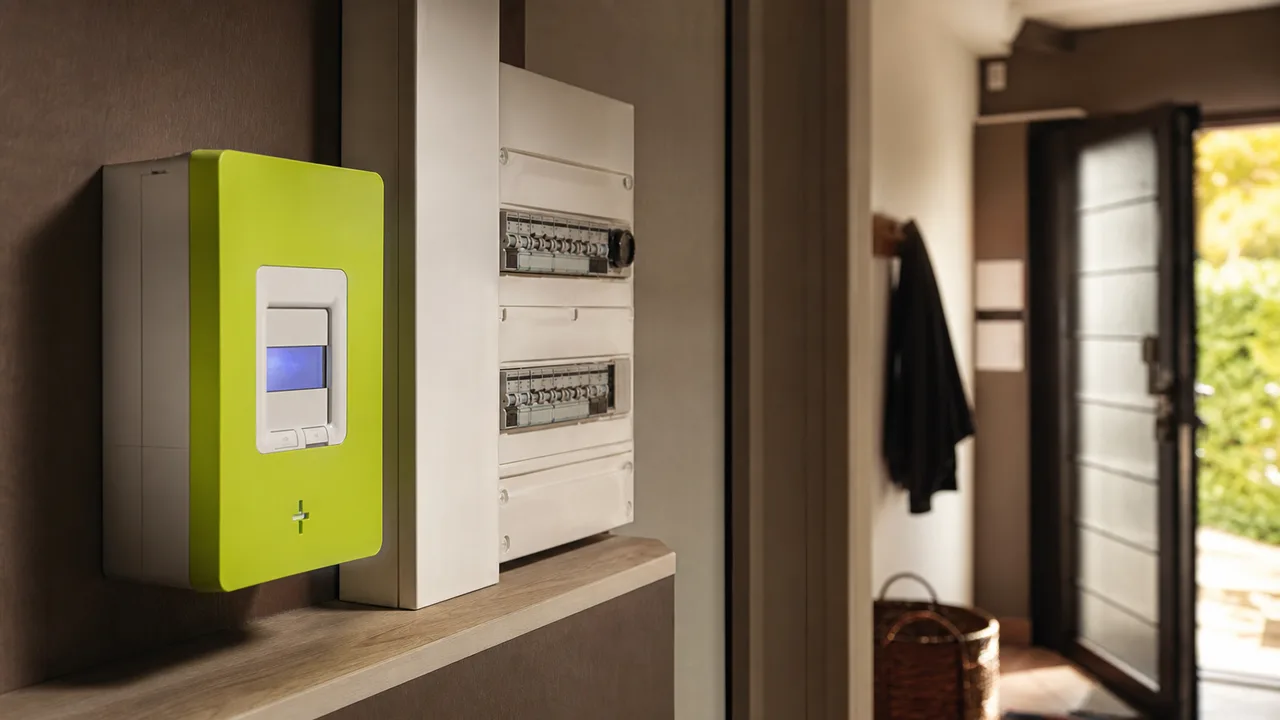 Compteur électrique Linky fixé au mur d'un couloir, écran affichant des chiffres, lumière naturelle douce
